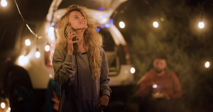 Friends enjoy time together outside under lights, sharing laughs, taking pictures, and relaxing by a car in the evening during a gathering
