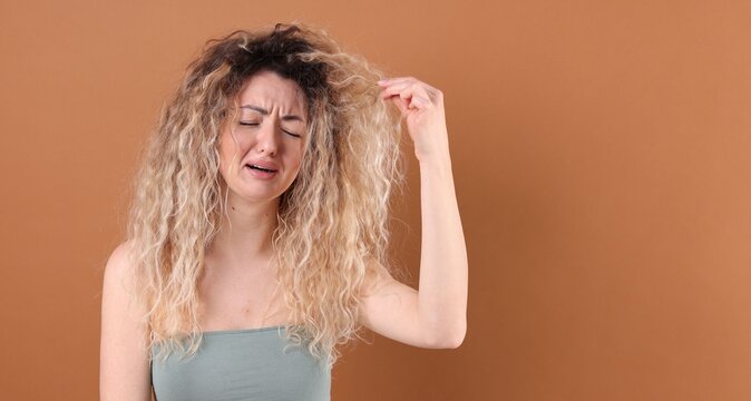 Unhappy woman with tangled damaged hair on brown background, space for text