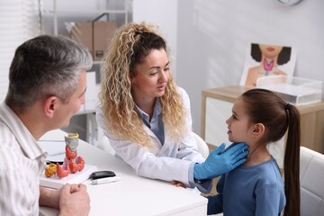Fototapeta na wymiar Endocrinologist in medical gloves examining girl's thyroid gland while her father supporting her at white desk in clinic