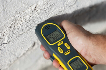 Moisture Meter measuring the moisture level of an exterior wall of a house, close up hand  © Devka