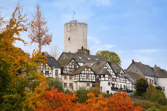 Historic view of Reifferscheid with white castle tower and traditional half-timbered houses. Autumn foliage and clear sky, Eifel region, Germany