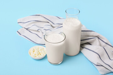 Glass of fresh kefir and bowl with cottage cheese on blue background