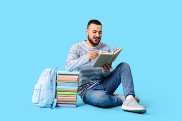 Fototapeta premium Male student with stack of books sitting on blue background