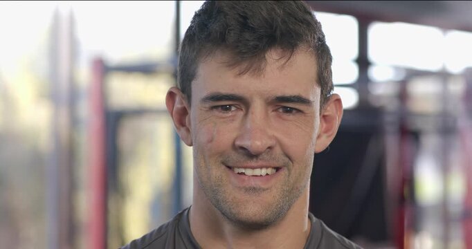 Adult male athlete standing in gym letting tear roll down cheek before smiling broadly in relief