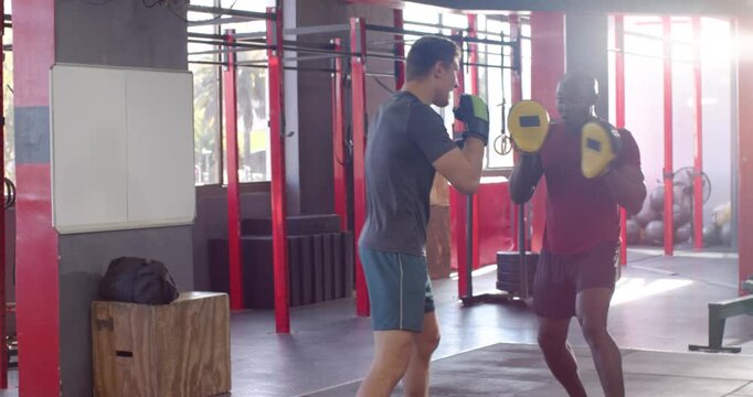 Tapping focus pads, male trainer and male trainee practicing jab cross hook combos at boxing gym