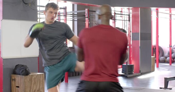 Male gloved athlete kicking and punching coach-held shields to refine precision in gym