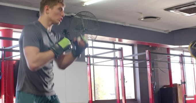 Diverse male coach with mitts guiding trainee throwing combos pivoting, refining form