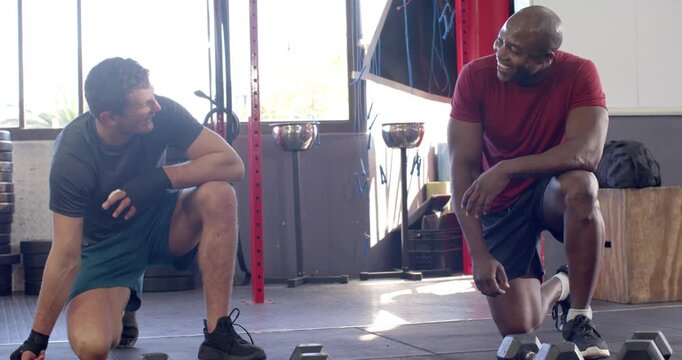 African american trainer instructing white trainee in dumbbell pushups and stretching upward