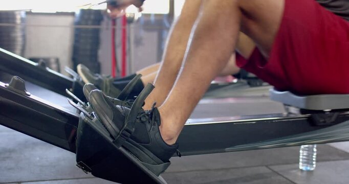 Diverse male rowers adjusting straps then pulling handles for rowing gym workout