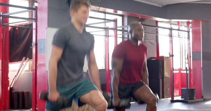 Post-warm-up male training duo stepping into lunges holding dumbbells at gym to build strength
