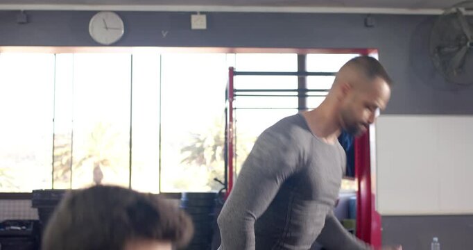 Diverse male friends gripping kettlebells at gym hinging and swinging overhead for strength