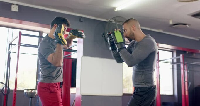 Trainer raising focus mitts signalling indian trainee throwing punches at boxing gym training