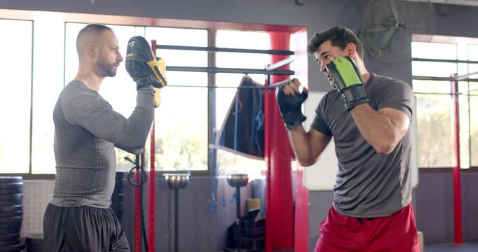 Diverse male duo practicing boxing combinations at gym corner wearing gloves and mitts