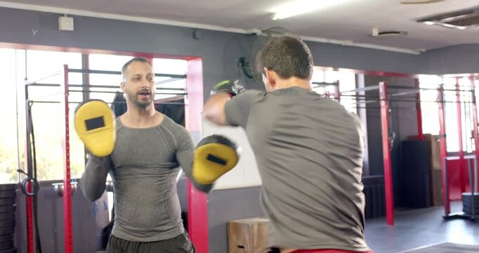 Diverse trainer and trainee responding to combo calls by punching mitts in gym drill