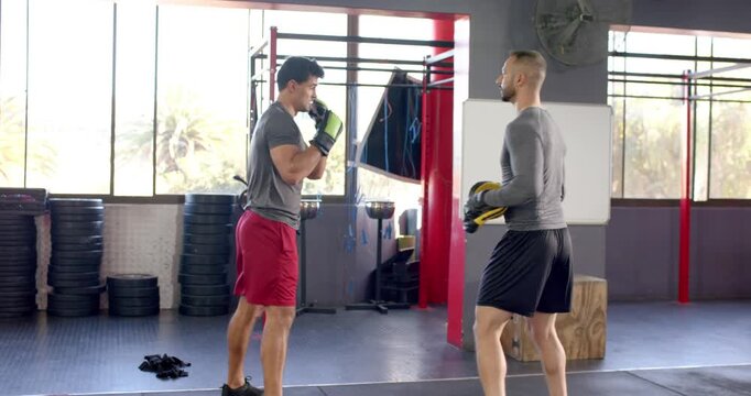 White male coach raising focus mitt and guiding indian male trainee throwing jab-hook combos
