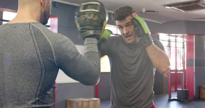 White coach shifting focus mitts and indian trainee throwing combo at gym building speed accuracy