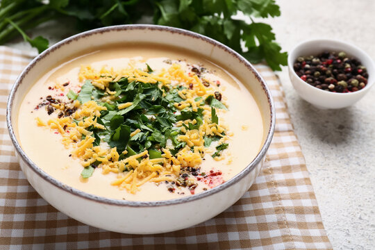 Bowl of tasty cheese soup with parsley and peppercorns on white background, closeup
