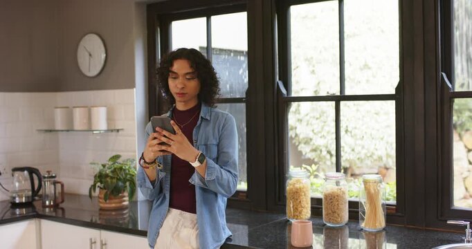 Non-binary person tapping smartphone checking messages at kitchen counter watching outside window