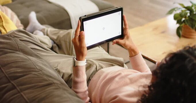 Non-binary person reclining on couch at home tapping blank tablet screen, swiping, browsing content