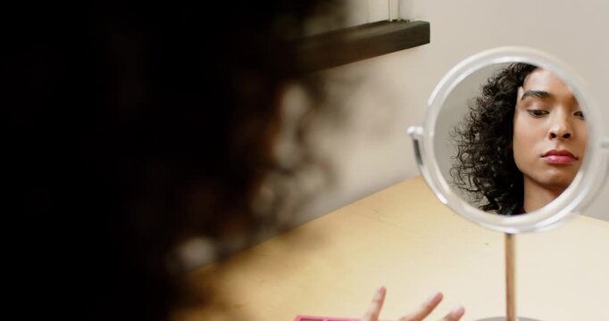 Non-binary person picking up spoolie and pencil at vanity mirror grooming brows for defined arches