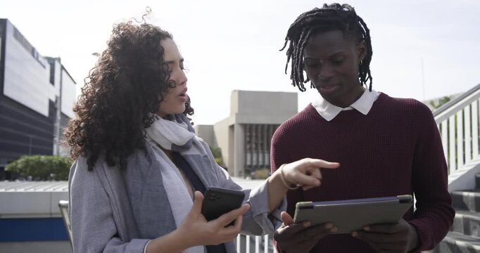 Diverse coworkers pointing phone screen, gesturing and discussing tablet on rooftop terrace