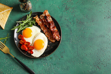 Naklejka premium Plate with tasty fried eggs, bacon and tomatoes on green grunge background