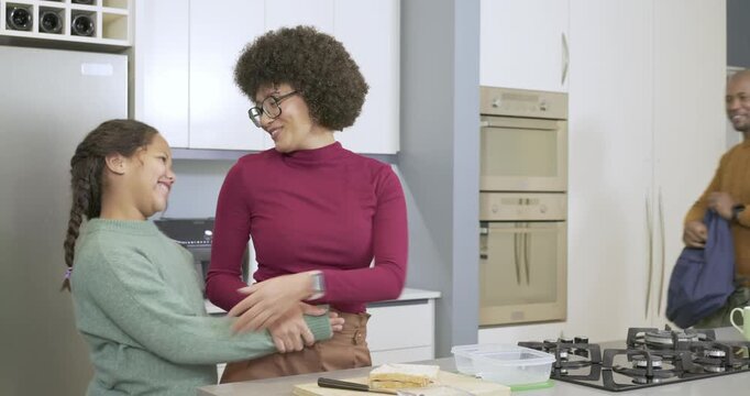 Woman slicing banana toast on kitchen island, daughter hugging her, dad unzipping backpack