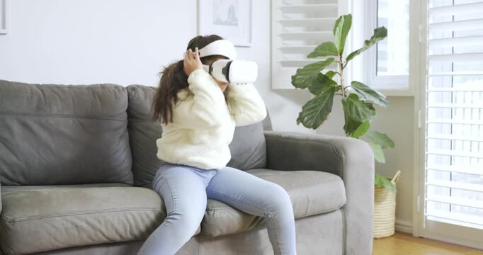 Female child tapping VR gear initiating game, swatting objects adjusting headset concluding on sofa