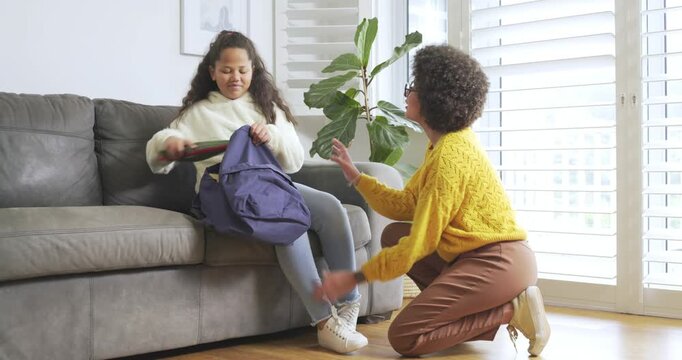 African American mother and daughter getting book from bag tying shoe hugging pumping fists at home