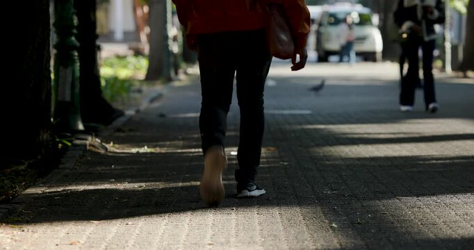 Man in orange coat walking into frame carrying bag on sidewalk toward car, pigeon
