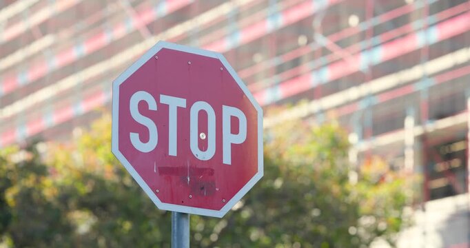 Red octagonal STOP sign remaining centered on post at sunny corner while woman crossing sidewalk