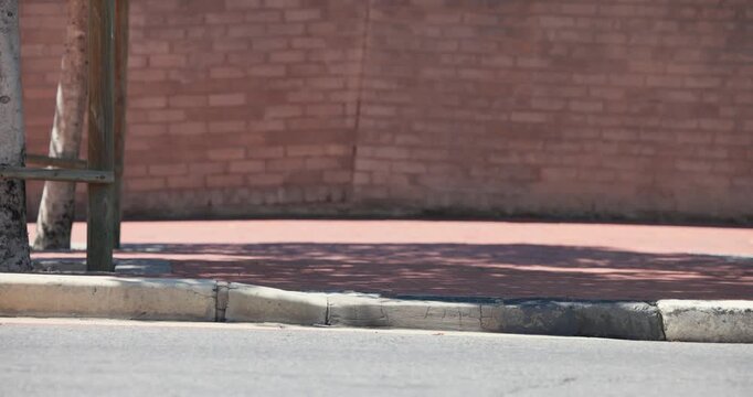 Empty curb and pink path are staying still until pedestrians enter, walking past brick wall onward