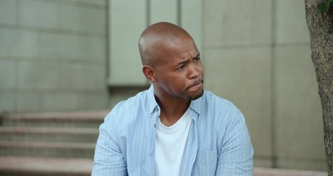 African man sitting on bench holding cup, inspecting, smiling, sipping, responding to off-frame cue