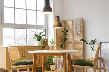 Fototapeta premium Interior of stylish dining room with table, houseplants, big window and glowing lamp
