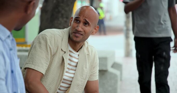 Diverse male friends bald man leaning forward replying to left friend query on bench with bracelets