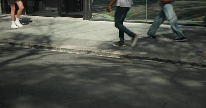 Diverse pedestrians entering from left, walking across sidewalk by reflective glass, heading onward