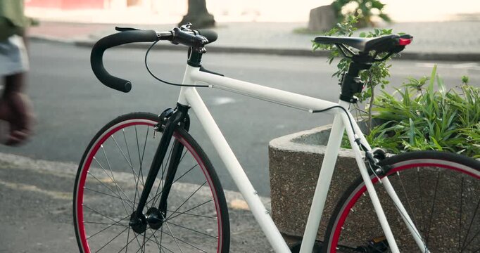 Returning green-shirt man is lifting white fixie from planter and wheeling it into street to ride