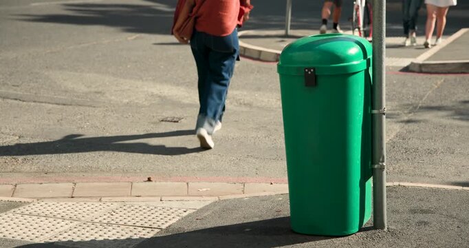 Green bin is standing at corner after cyclist is passing, people are crossing to reach sidewalk