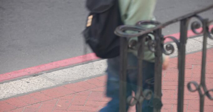 Diverse people entering left, walking past iron rail and red curb, carrying backpacks, copy space