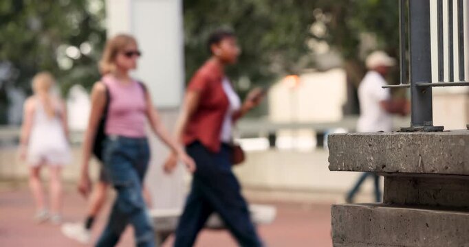 African American woman on bench in plaza using phone, seeing walkers, standing and walking by slabs