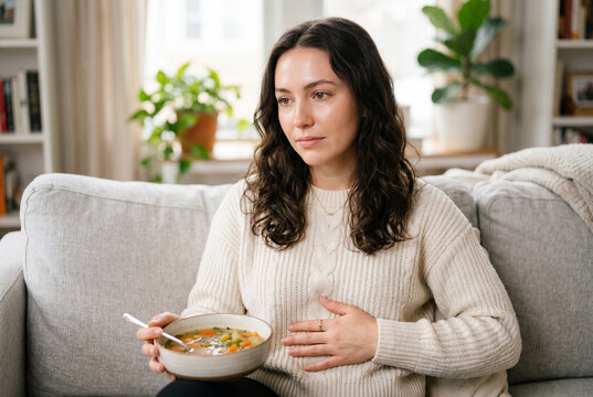 Woman holding soup bowl and touching stomach with mild discomfort