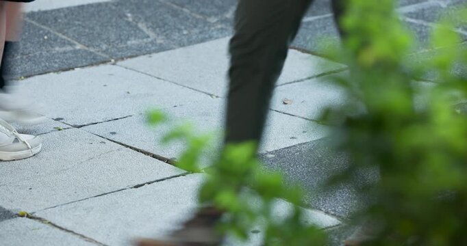 Tiled sidewalk is showing passing feet with white sneaker stepping in, pedestrians walking to work