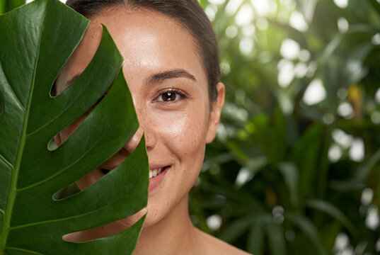 Natural woman covering one eye with green monstera leaf