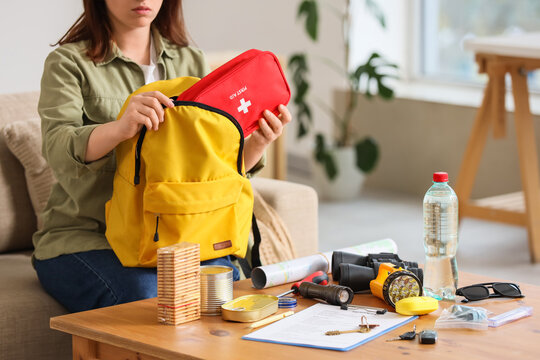 Woman packing emergency backpack with necessities at home