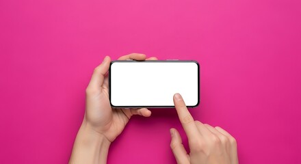 Obraz premium Person's hands holding a modern smartphone horizontally with a blank white screen, finger touching the display against a vibrant magenta backdrop, top-down view.