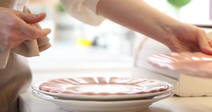 Woman wiping plates with pink napkin at white table against blurred background, closeup
