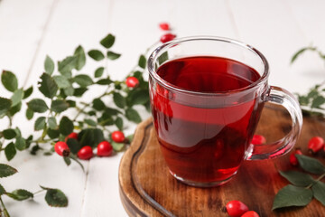 Glass cup of hot rose hip tea and berries on white wooden background, closeup