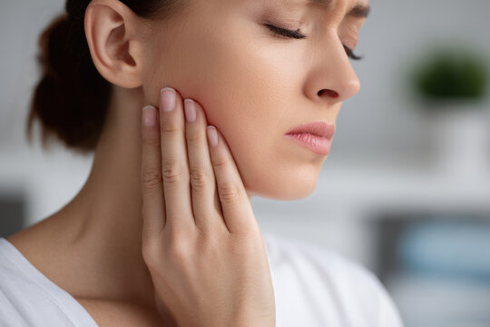Woman holding jaw in pain with closed eyes showing toothache and facial discomfort while touching cheek