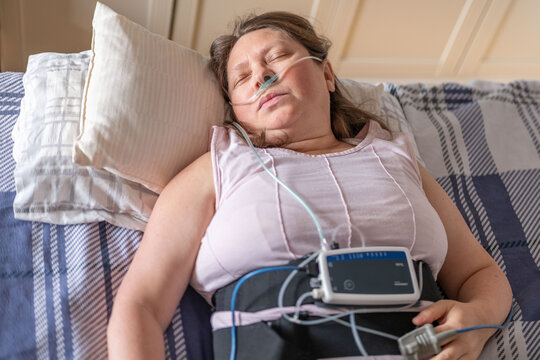 Woman resting in bed with home medical monitoring device, nasal cannula oxygen, apnea monitoring, pulse oximeter home healthcare, COPD quiet recovery, screening and treatment chronic sleep deprivation