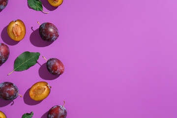 Obraz premium Fresh ripe plums and leaves on purple background